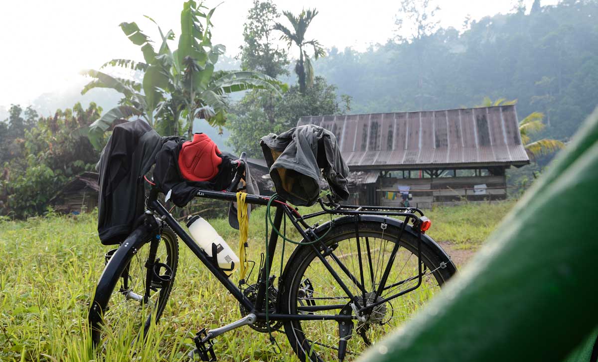 Die letzten zwei Stunden im Regen gefahren. Da wieder kein Platz zum Campen in der Natur zu finden war, fragte ich an, ob es wohl möglich sei, hinter dem Haus mein Zelt aufzuschlagen. Der junge Mann zeigte sich nicht abgeneigt, wollte aber erst die Zustimmung des Dorfvorstandes einholen. Gemeinsam besuchten wir sein aus Holzlatten zusammengezimmertes Haus, dessen Wände innen mit Zeitungspapier tapeziert waren. Eine Stereo-Anlage mit riesigen Lautsprechern dominierte das Innere. Schlotternd beantwortete ich seine Fragen. Die Stimmung war eher ernsthaft. Schließlich gab er lächelnd sein okay, und fragte mich, ob ich in meinem Land nicht genug Probleme hätte, dass ich hier her käme, um Rad zu fahren....